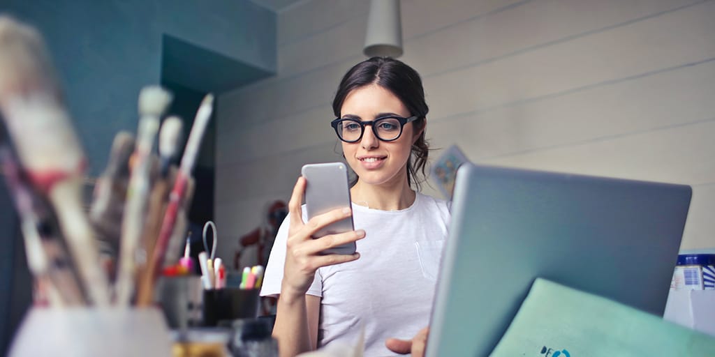 Girl looking at email on her phone while on a computer